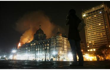 <p>A reporter talks on her phone as smoke is seen coming from Taj Mahal hotel in Mumbai November 27, 2008. (REUTERS)</p>