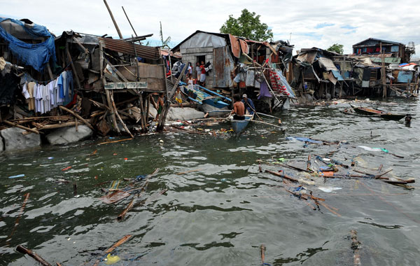Filipino paddle their boat in front of shanties damaged by Typhoon Conson along a brake water in Manila.Troops scoured jagged coastlines on the Philippines' eastern seaboard in search of dozens of fishermen who went missing after a ferocious typhoon battered the country, killing 23 people.(AFP)