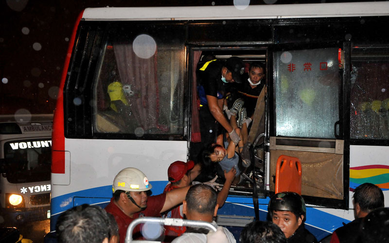 Paramedics (top) lower a victim from the hijacked bus in Manila. The gunman who seized a bus carrying Hong Kong tourists killed at least four of his hostages in the Philippines, doctors said. (AFP)