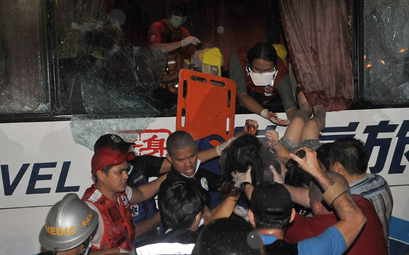 A paramedic (top) lowers one of the wounded survivor from the hijacked bus in Manila. (AFP)