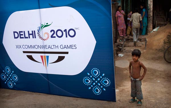 A child stands next to a board advertising the Commonwealth Games in New Delhi, India. (AP)