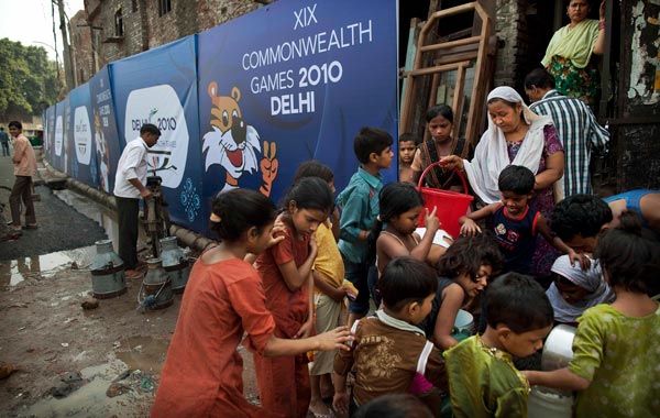 Children and women fill containers at a water collection point next to boards advertising the Commonwealth Games in New Delhi, India. (AP)