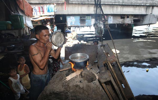 A Filipino living under a river bridge, an area prone to damage and flood from typhoons, cooks a meal for his family in Manila, Philippines. (EPA)