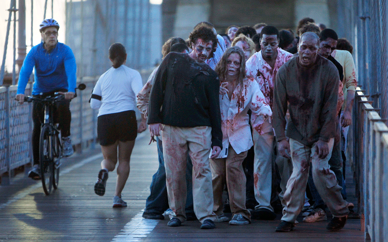 A bicyclist and jogger pass a group of zombies posing for pictures on the Brooklyn Bridge in New York.  The stunt was part of a campaign in 26 cities worldwide promoting the Halloween premiere of the AMC television series "The Walking Dead." (AP)