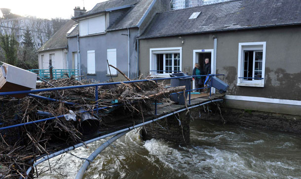 Residents stand in their doorway as they look at debris on a bridge the day after flooding from melting snow hit Cherbourg. (REUTERS)