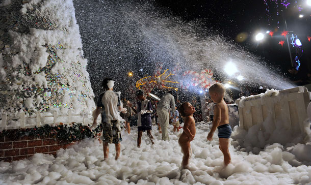 Children play with foam created as snow outside a shopping mall in Singapore. Most shopping malls are decorated with colourful lights, ornaments and figurines to mark the forthcoming festive season. (AFP)