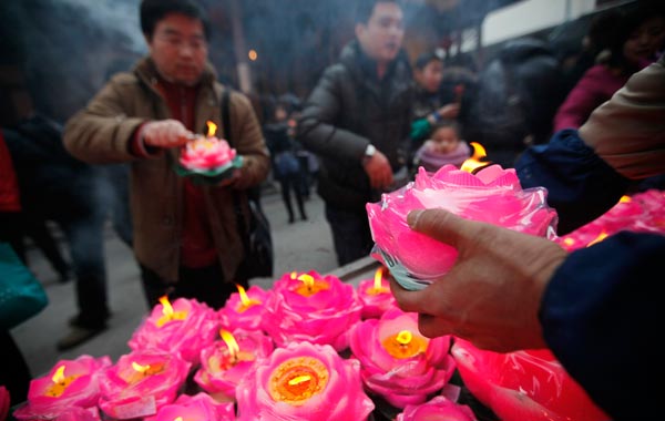 A temple worker, right, arrange the lotus flower shape candles set by worshippers at a temple to mark the New Year celebrations in Shanghai, China. (AP)