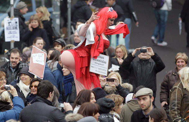 A woman on stilts mocking a prostitute amuses people marching against Italian premier Silvio Berlusconi during a protest in Milan, Italy. Thousands of women turned out in 200 Italian cities to denounce what they say is Berlusconi's debasing of females. Prosecutors want to try Berlusconi for allegedly paying a 17-year-old Moroccan girl for sex. Paying for prostitution with a minor is a crime in Italy. Berlusconi and the teenager have denied the allegation. The banner she wears reads: "New dictionary of the Italian society. Adjourned edition 2011. Woman: inert support for television boobs and asses" (AP)
