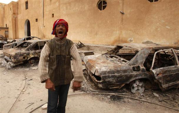 A man gestures in front of burnt vehicles in a state security building in Tobruk, eastern Libya February 24, 2011. (REUTERS)
