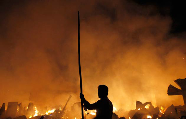 A local resident walks with a stick as he tries to help put out a fire in a slum in Mumbai. (REUTERS)