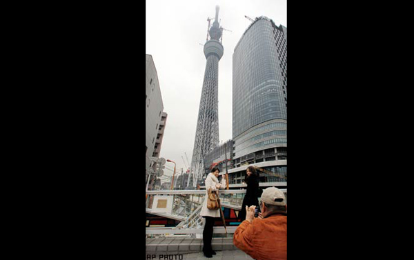 People pose for a photo with Tokyo Sky Tree, a new landmark tower still under construction in Tokyo, March 1, 2011. Designed by award-winning Japanese architect Tadao Ando and sculptor Kiichi Sumikawa, the tower stands on a triangular foundation. (AP)