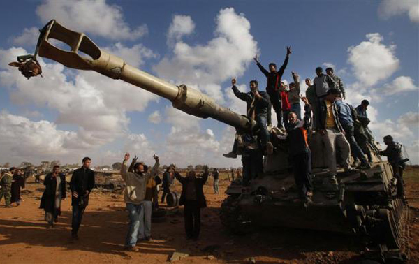 People celebrate atop a destroyed mobile artillery piece belonging to forces loyal to Libyan leader Muammar Gaddafi after an air strike by coalition forces, along a road between Benghazi and Ajdabiyah. (REUTERS)