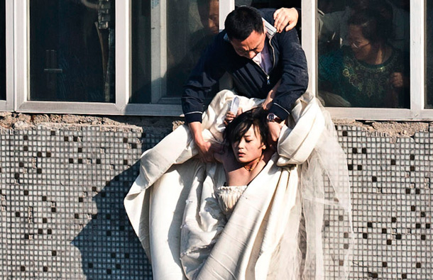 A 22-year-old woman in a wedding gown is grabbed by Guo Zhongfan, a local community officer, as she attempts to kill herself by jumping out of a seven-storey residential building in Changchun, Jilin province. (REUTERS)