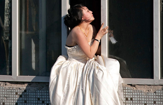 A 22-year-old woman in a wedding gown sits on a windowsill before attempting to kill herself by jumping out of a seven-storey residential building in Changchun, Jilin province. (REUTERS)