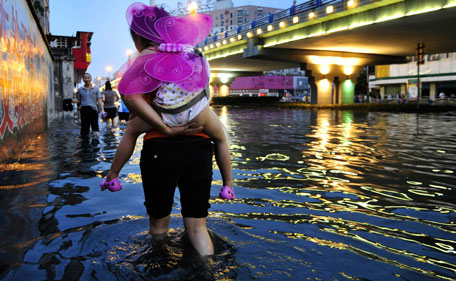 A resident carries a child on her back as she walks on a flooded street after heavy rainfalls in Chengdu, Sichuan province, July 3, 2011. Heavy downpour hit Chengdu on Sunday, flooding roads and breaking down city traffic. Warnings of further rainstorms and possible floods or landslides have been released, Xinhua News Agency reported.  (REUTERS)