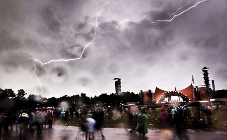 Lightning flashes across the sky as spectators wrap up during the annual Roskilde music festival on July 3, 2011. (AFP)