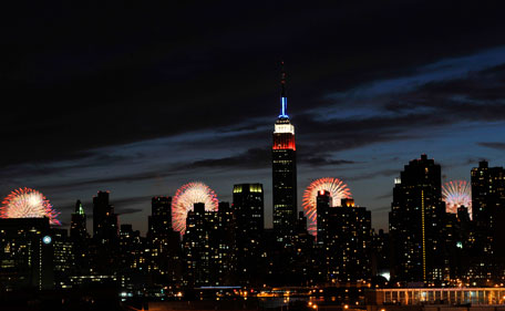 The Empire State Building, illuminated with red, white and blue lights, is seen from across the East River in the Queens borough of New York, backlit by fireworks exploding over the Hudson River, during the Macy's Fourth of July fireworks show on Monday, July 4, 2011 in New York. (AP)