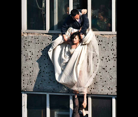 A 22-year-old woman in a wedding gown is grabbed by Guo Zhongfan, a local community officer, as she attempts to kill herself by jumping out of a seven-storey residential building in Changchun, Jilin province. (REUTERS)