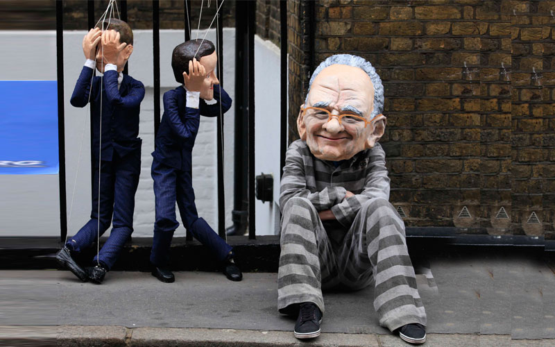 A protester wearing a caricature giant head depicting News Corporation CEO Rupert Murdoch sits next to puppets of Britain's Prime Minister David Cameron outside Murdoch's apartment in central London. The British parliament will unite on Wednesday to urge Rupert Murdoch to drop plans to further expand his media empire in a move unthinkable before a phone hacking scandal exploded just two weeks ago. (REUTERS)