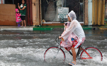 Residents ride a bicycle through a flooded street in Las Pinas, Metro Manila July 26, 2011. More than 100,000 families were displaced due to flooding, while 11 fishermen were missing in central Philippines as Typhoon Juaning battered the main Luzon island, forcing schools to close and grounding domestic flights and ferry services, disaster officials said on Tuesday.  (REUTERS)