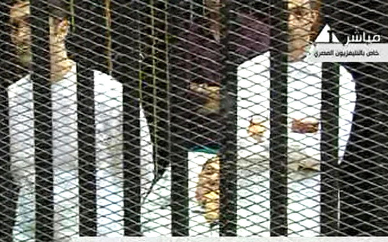 This video image taken from Egyptian State Television shows 83-year-old Hosni Mubarak laying on a hospital bed inside a cage of mesh and iron bars as he flanked by his sons Alaa, left, and  Gamal right,  in a Cairo courtroom as his historic trial began on charges of corruption and ordering the killing of protesters during the uprising that ousted him. The scene, shown live on Egypt's state TV, was Egyptians' first look at their former president since Feb. 10, the day before his fall when he gave a defiant speech refusing to resign. (AP)