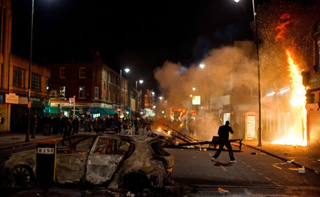 A shop and police car burn as riot police try to contain a large group of people on a main road in Tottenham, north London on August 6, 2011.  Two police cars were on Saturday set ablaze in north London following a protest over the fatal shooting of a 29-year-old man in an armed stand-off with officers.  The patrol cars were torched as dozens gathered outside the police station on the High Road in Tottenham. (AFP)