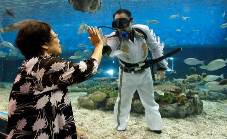 A visitor gives a high five to a professional diver wearing an Elvis Presley attire inside an aquarium of the Ocean Park in Manila August 15, 2011. Presley, the "King of Rock and Roll", died at his home, Graceland Mansion, in Memphis, Tennessee, at the age of 42 on August 16, 1977 from drug overdose. (REUTERS)