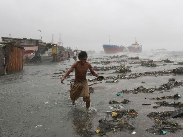 A resident flees from strong winds as an oil tanker in background is battered by big waves after it broke off its anchor and slammed a row of shanties at the height of typhoon Nesat Tuesday Sept. 27, 2011 in the Philippines. (AP)