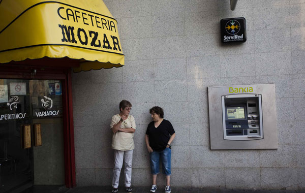 Women talk as one of them smokes next to an ATM machine of a branch of Spain's lender bank Bankia in Madrid June 25, 2012. Spain formally requested European aid for its indebted banks on Monday but the lack of details rekindled investor doubts over the financial sector, hours before Moody's was expected to cut the ratings of all Spanish lenders.  (REUTERS)