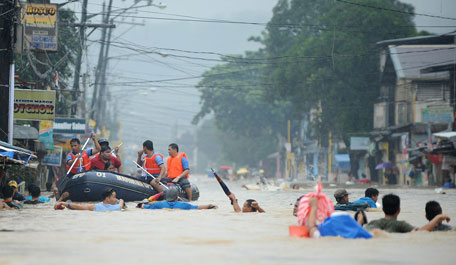 People wade through a flooded street under heavy rains as rescuers on a rubber boat evacuate residents from their  homes in the village of Tumana, Marikina town, in suburban Manila. (AFP)
