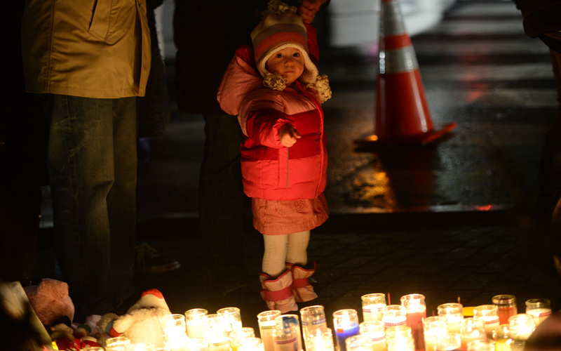 A young child points at candles as people pay their respects at a makeshift shrine to the victims of a elementary school shooting in Newtown, Connecticut.  A young gunman slaughtered 20 small children and six teachers on December 14, 2012 after walking into a school in an idyllic Connecticut town wielding at least two sophisticated firearms. (AFP)