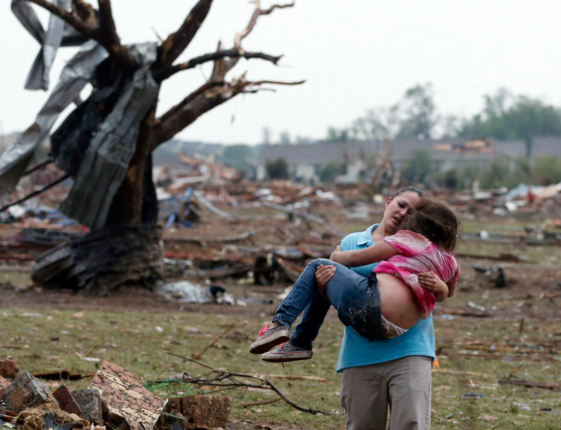 A woman carries a child through a field near the collapsed Plaza Towers Elementary School in Moore, Okla., Monday, May 20, 2013. The relationship between the woman and the child was not immediately known. A tornado as much as half a mile (.8 kilometers) wide with winds up to 200 mph (320 kph) roared through the Oklahoma City suburbs Monday, flattening entire neighborhoods, setting buildings on fire and landing a direct blow on an elementary school. (AP)