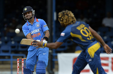 Indian captain Virat Kohli (left) plays a shot as Sri Lankan bowler Lasith Malinga fields during the sixth match of the Tri-series at the Queen's Park Oval stadium in Port of Spain on July 9, 2013. (AFP)