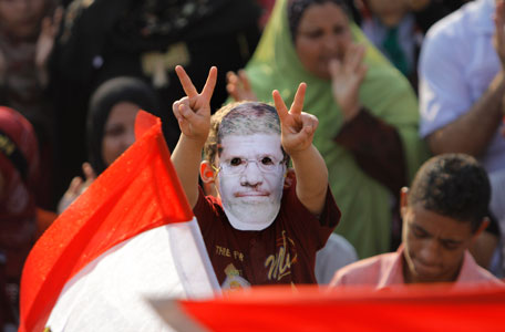 A Supporter of Egypt's ousted President Mohammed Morsi flashes victory signs as he puts on a mask with his picture during a protest in Nahda Square, where protesters have installed their camp near Cairo University in Giza, in southwestern of Cairo, Egypt, Tuesday, Aug. 13, 2013. Egypt's interim president swore in 20 new provincial governors on Tuesday, a move that reinforces the new leadership's authority and removes all Muslim Brotherhood members previously installed in the posts by Mohammed Morsi before his ouster as president. (AP)