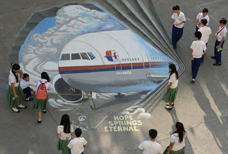 Students stand next to a giant mural featuring missing Malaysia Airlines flight MH370 displayed on the grounds of their school in Manila's financial district of Makati on March 18, 2014, created as part of solidarity action by concerned artists for the passengers and crew of the missing plane. Three million people around the world have joined an effort led by a satellite operator to locate the missing Malaysia Airlines plane, in what may be the largest crowdsourcing project of its kind. The plane went missing early on March 8 with 239 passengers and crew aboard, spawning a massive international search across Southeast Asia and the Indian Ocean that has turned up no trace of wreckage.  (AFP)
