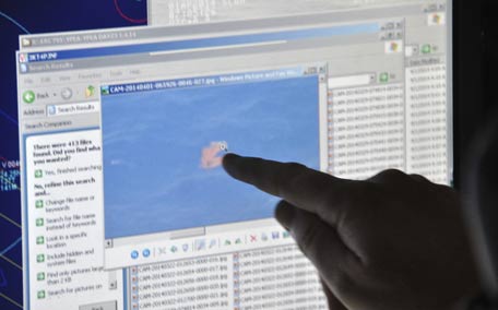 Royal New Zealand Air Force crewman aboard a RNZAF P-3 Orion Rescue Flight 795 points to an image of an orange object floating on the ocean which was photographed moments earlier and uploaded onto the plane's computer system during a search for debris from the missing Malaysia Airlines Flight MH370 in southern Indian Ocean. (AP)