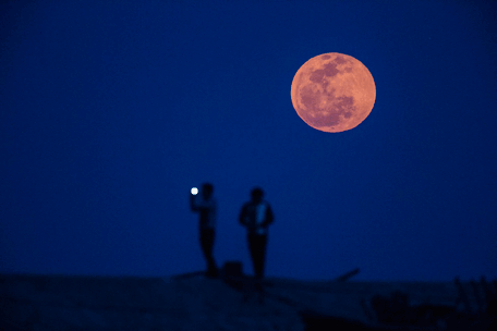 A man takes a picture during moon rise in a suburb of Shanghai April 15, 2014. (REUTERS)