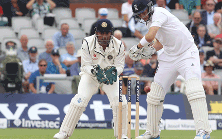 India captain Mahendra Singh Dhoni (L) looks on as England's Joe Root plays a shot during the second day of the fourth cricket Test match between England and India at Old Trafford in Manchester on August 8, 2014.     AFP