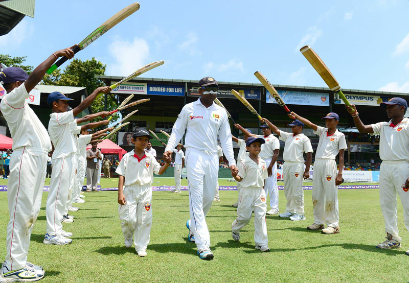 Sri Lanka cricketer Mahela Jayawardene (C) walks with children through an 'archway of cricket bats' as he goes out to field during the second day of the second Test match between Sri Lanka and Pakistan at the Sinhalese Sports Club (SSC) Ground in Colombo on August 15 [AFP]