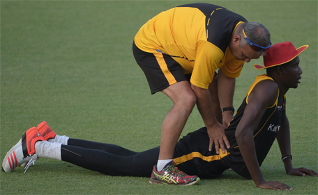 Zimbabwe cricketer Chris Mpofu (R) is helped to stretch by coach Dave Whatmore during a practice session at the Gaddafi Cricket Stadium in the Pakistani city of Lahore on May 20, 2015. (AFP)