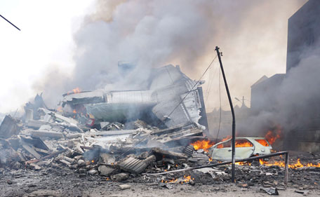 The charred tail section of an Indonesian military C-130 Hercules aircraft is seen amid wrecked houses and a burning car following a crash in Medan on June 30, 2015. An Indonesian military transport plane crashed on June 30 shortly after take-off in a city on Sumatra island, exploing in a ball of flames in a residential area. (AFP)
