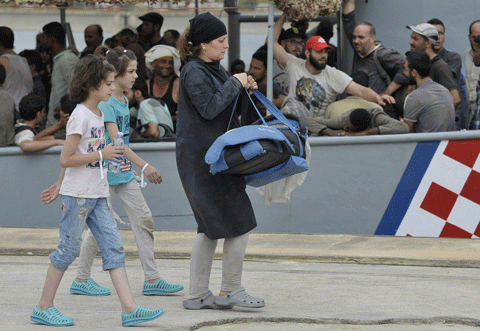 A woman carries a baby as she walks after disembarking from the Croatian Coast Guard ship SB72 Andrija Mohorovicic at the Augusta harbor, near Siracusa, Sicily, Italy, Sunday, Aug. 16, 2015. At least 40 migrants died Saturday in the hold of an overcrowded smuggling boat in the Mediterranean Sea north of Libya. (AP)